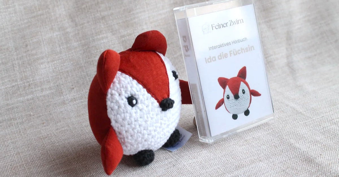 Handgehäkeltes Kuscheltier Fuchs Ida neben dem interaktiven Hörbuch von Feiner Zwirn – Geschenkset aus Kuscheltier und Hörbuch für Kinder